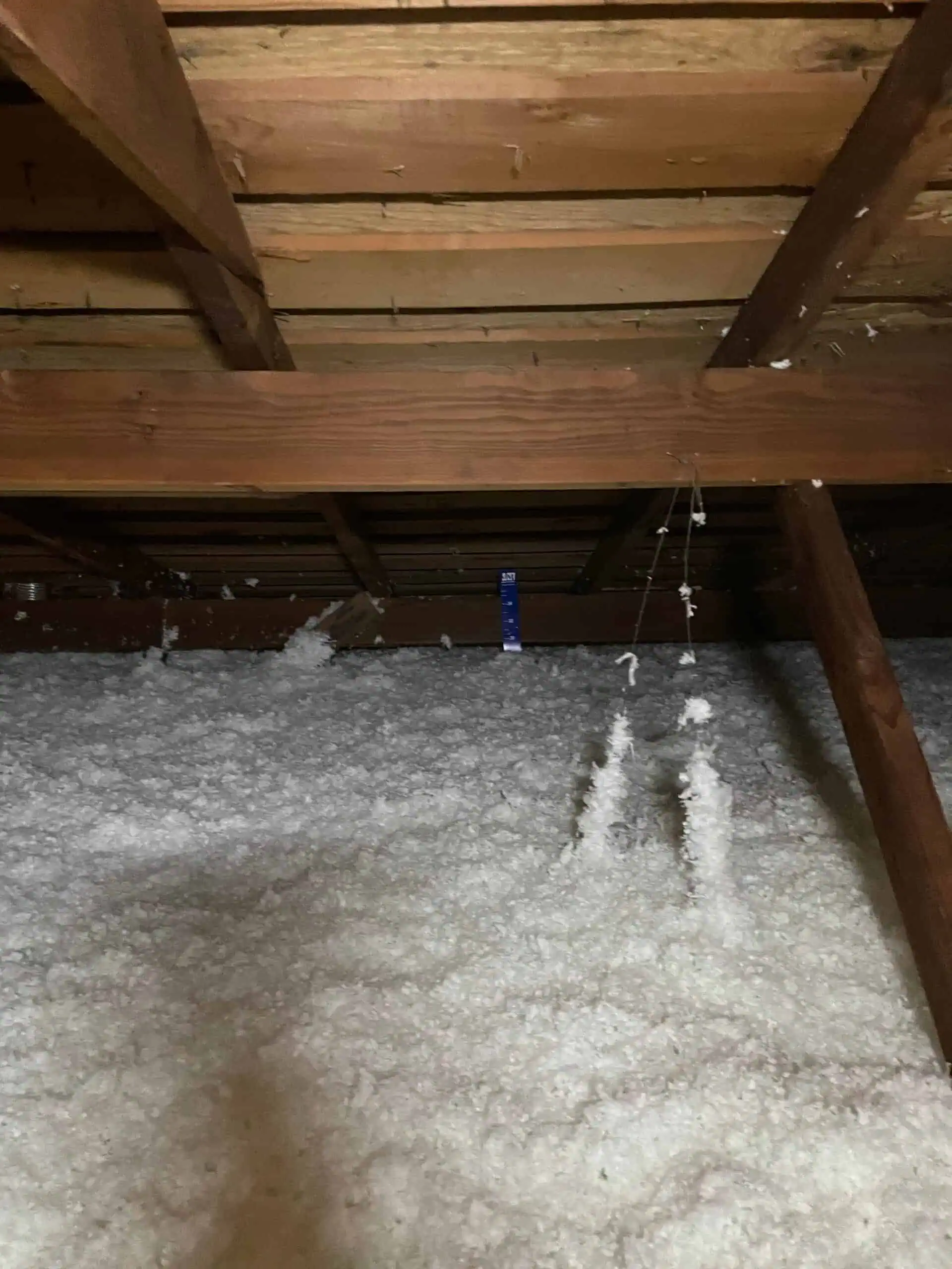 Insulation in attic space with wooden beams and spray foam insulation on the floor.