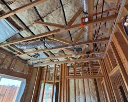 Insulation installation in a residential building under construction, showing wooden framing and duc.