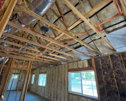 Insulation installation in a building with exposed framing and ductwork.